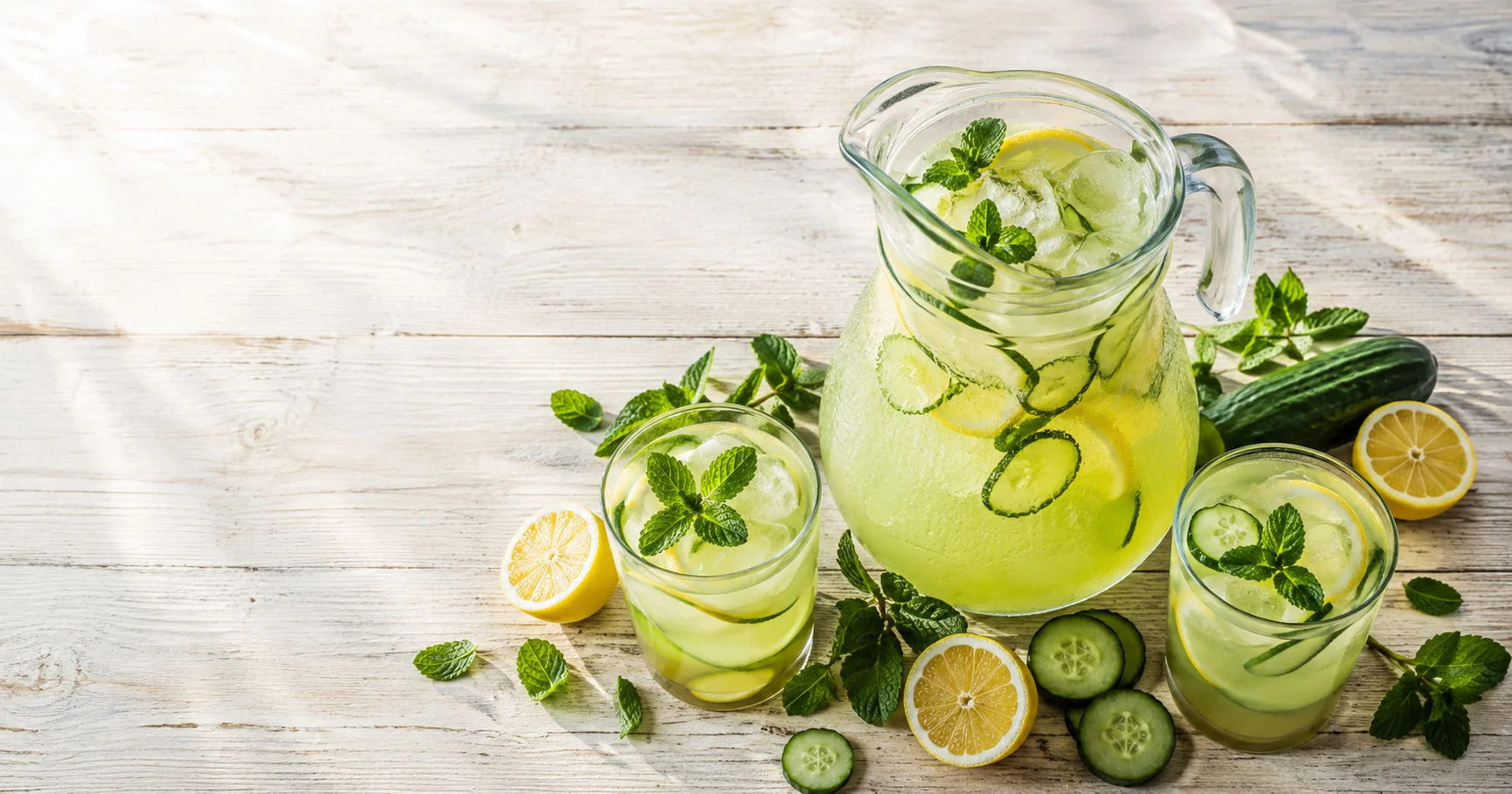 Pitcher and glasses of refreshing cucumber mint lemonade with ice and fresh mint garnish